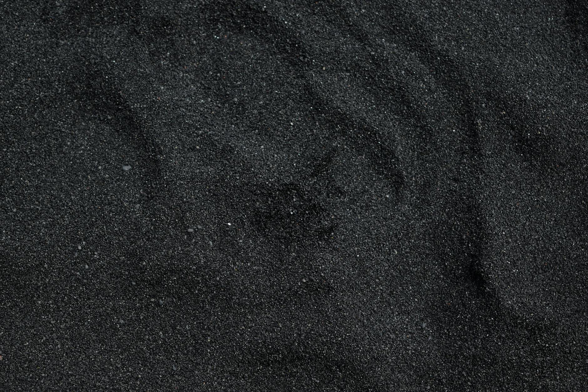 Close-up of fine black sand grains forming a dark, textured surface.