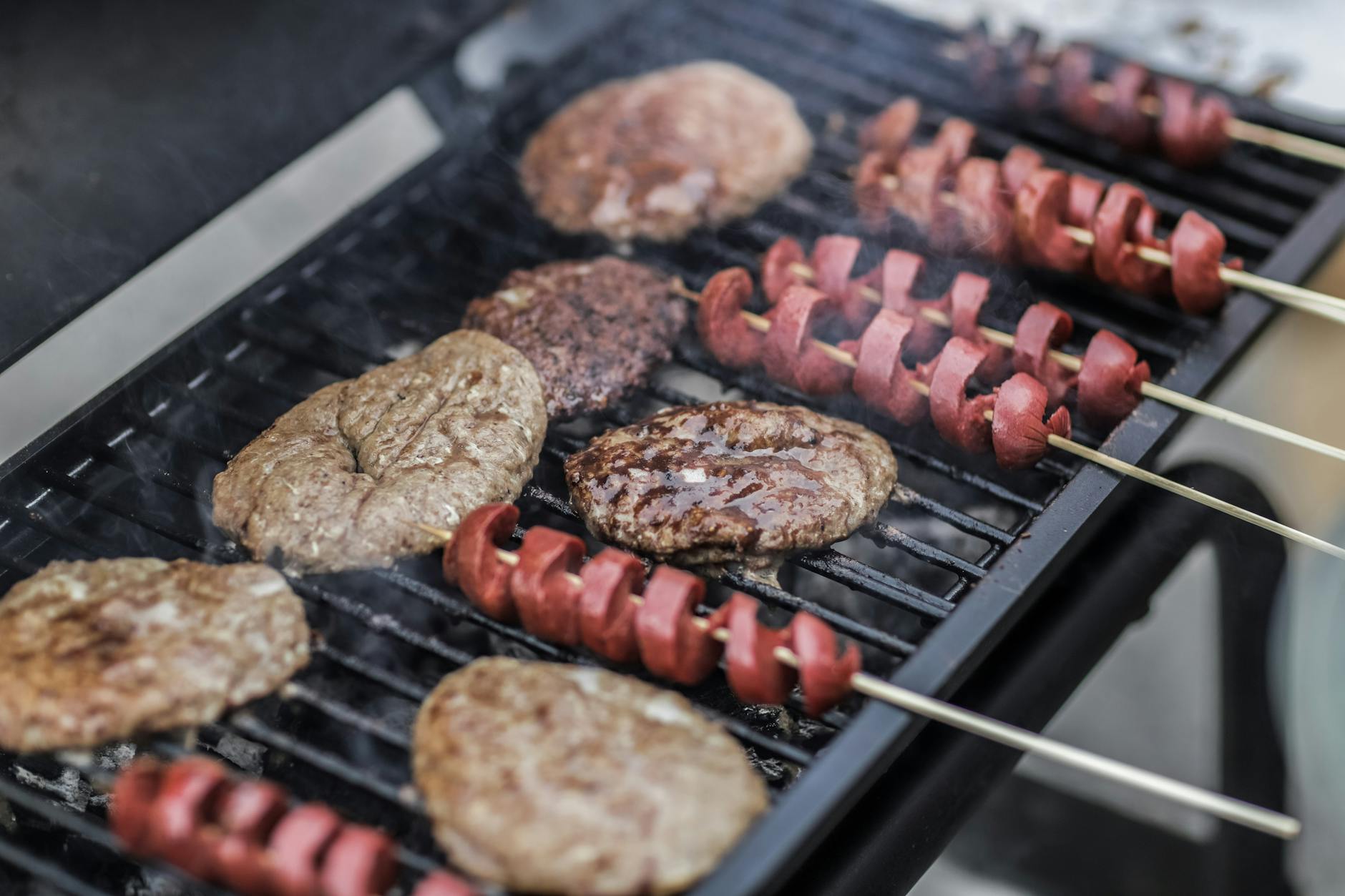 Grilled hamburgers and sliced hot dogs cooking on a barbecue grill over open flames