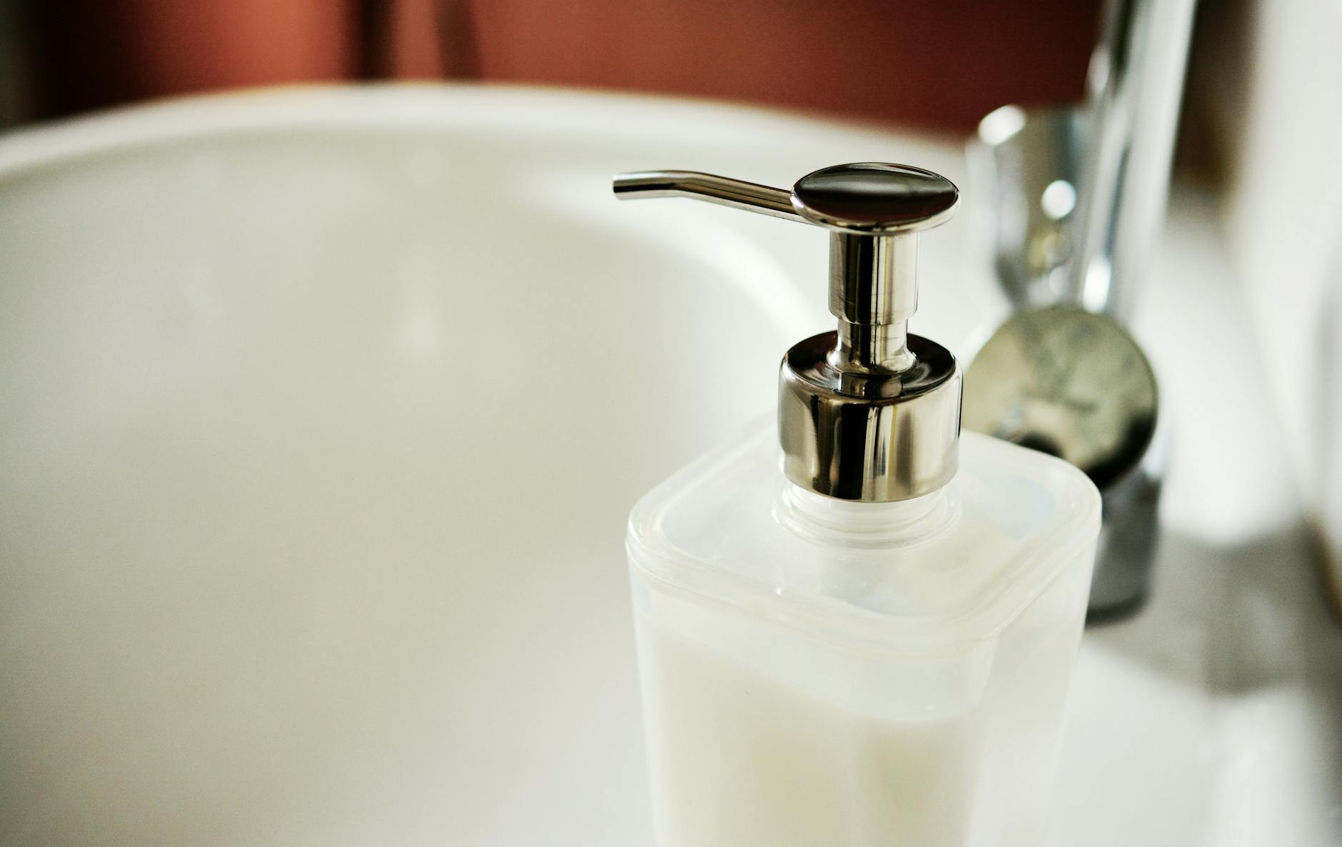 Close-up of liquid soap dispenser beside bathroom sink faucet, symbolizing hygiene and cleanliness