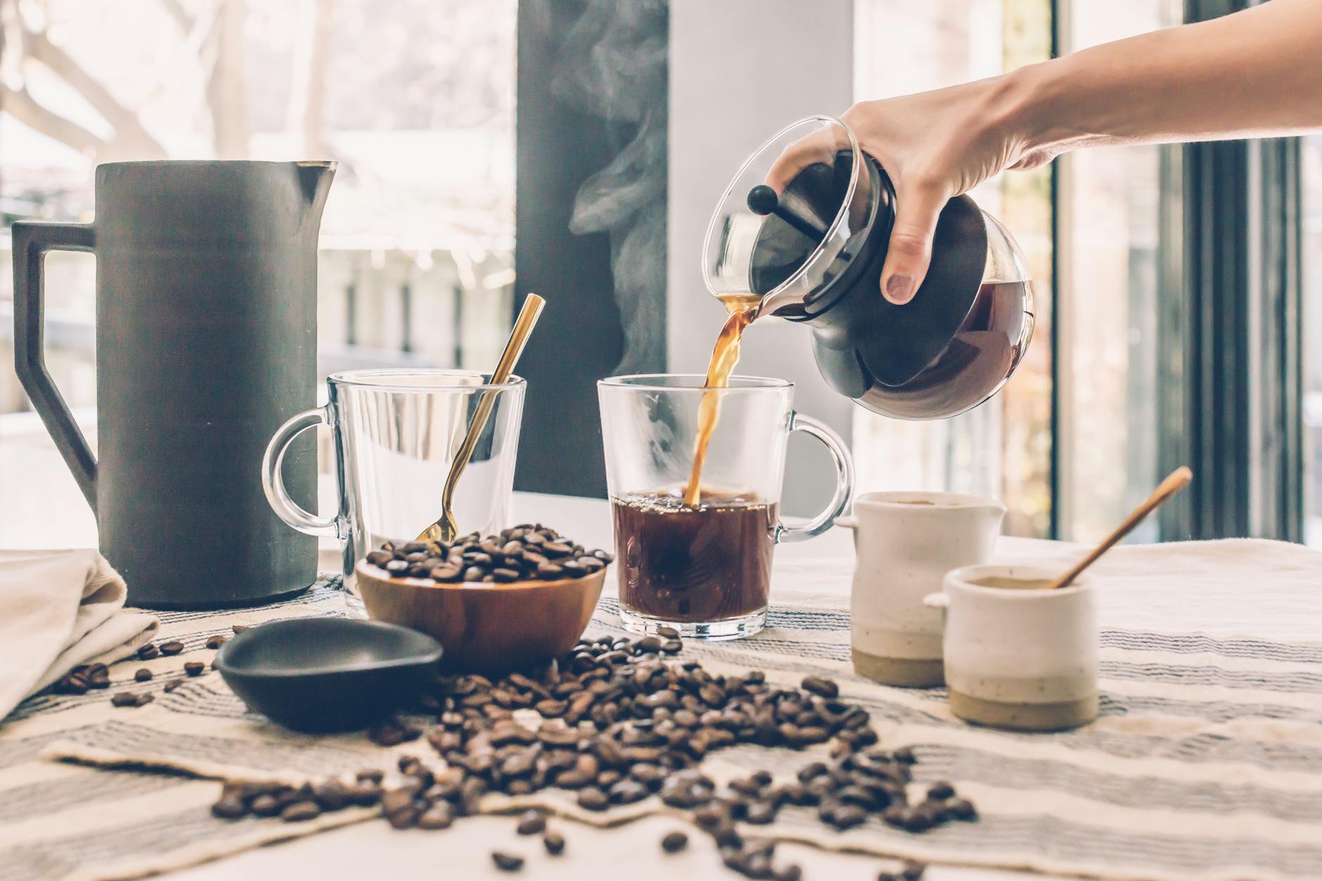 Freshly brewed coffee being poured into a glass cup on a cozy table with coffee beans and accessories