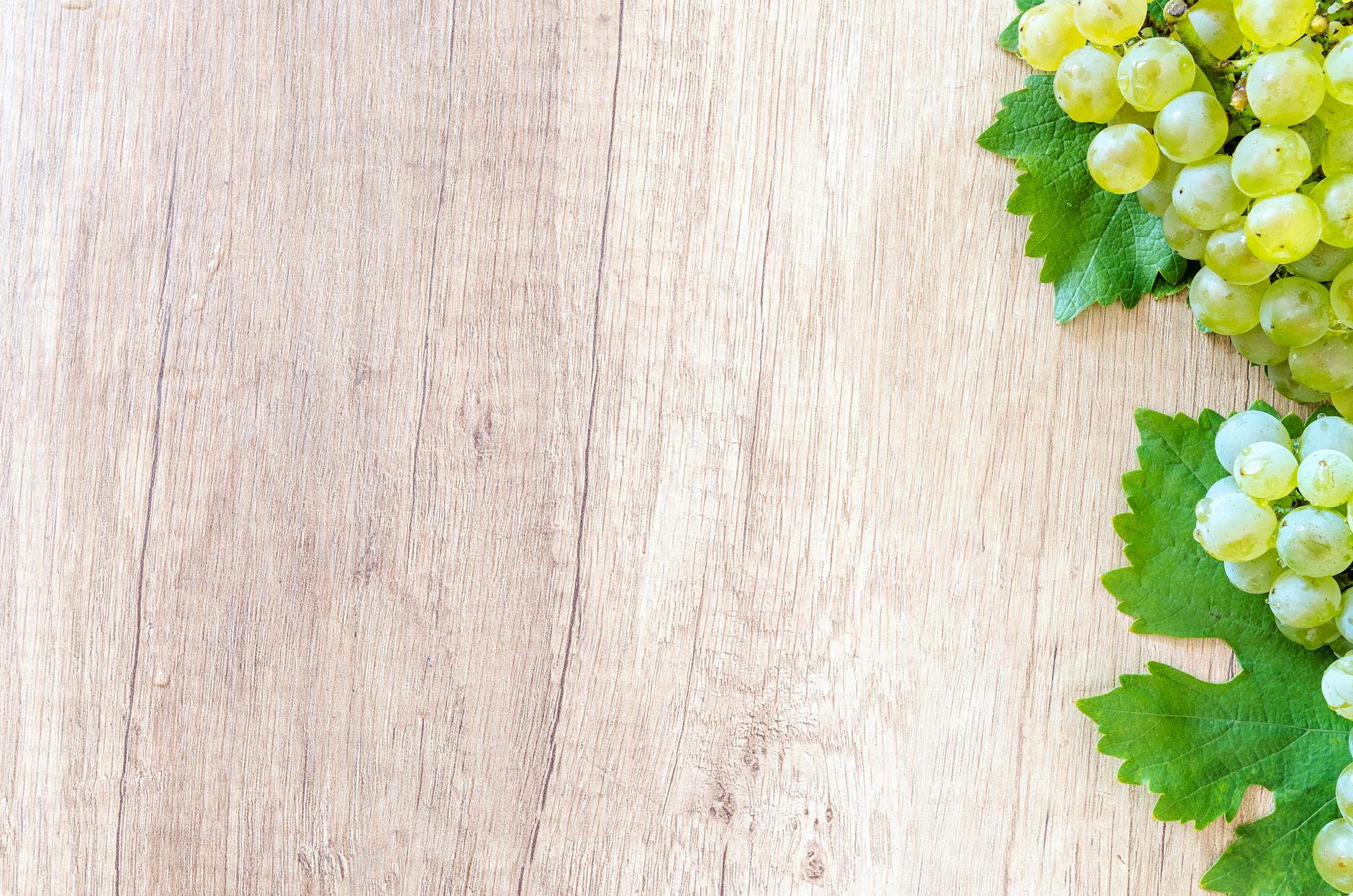 Fresh green grapes with leaves on a wooden table.